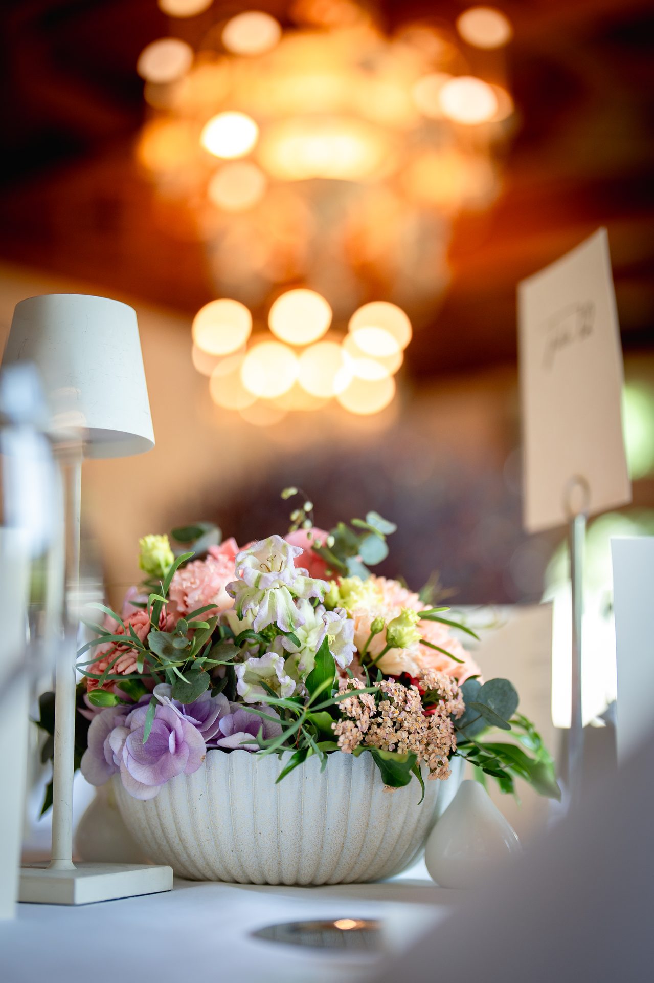 Sommerlicher Blumenstrauss in weisser Schale, Kronleuchter Bokeh – Tischdetails Lawyers Outing Villars